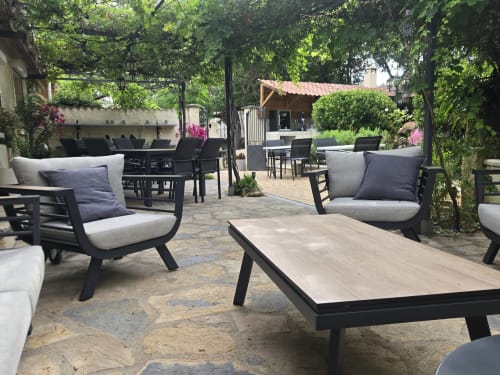 Terrasse ombragée à Domaine à l'Aise avec sièges longs noirs, tables en bois et verdure luxuriante à Saint-Pargoire