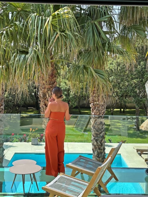 Femme en tenue rouge près de la piscine chauffée de la villa La Maison d'Ambrine à Chamaret, France, avec palmiers et transats