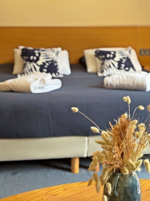Chambre de villa moderne à La Maison D'ambrine avec lit double, coussins décoratifs, fleurs séchées et murs aux teintes ambrées chaleureuses.