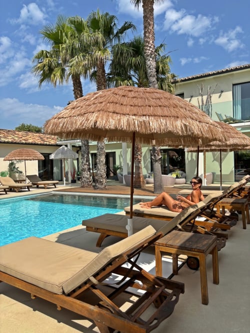 Zone piscine de La Villa Miami avec parasol en chaume, transats, palmiers et villa moderne à La Maison D'ambrine, Chamaret