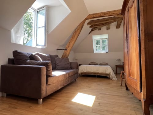 Grande chambre avec canapé, poutres, parquet, vue sur cour