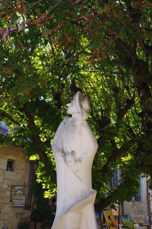 Buste en pierre blanche sous des arbres couverts de lierre dans la cour du village de Saint Germain et Mons