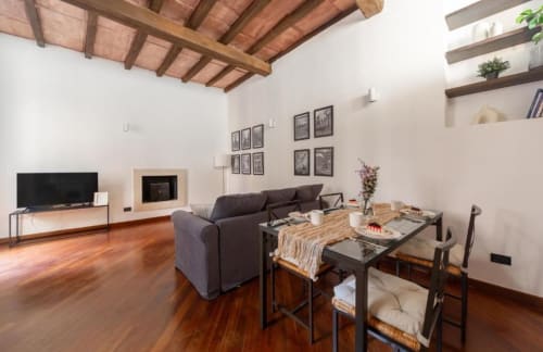 Wohnzimmer einer modernen Mailänder Wohnung mit Holzbalken, Parkettboden, grauem Sofa, Esstisch, Fernseher und Wandregalen.