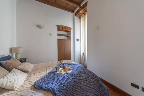 Gemütliches Schlafzimmer in den Magnolia Apartments Mailand mit blauer gesteppter Tagesdecke, Holzbalken und Stadtblick