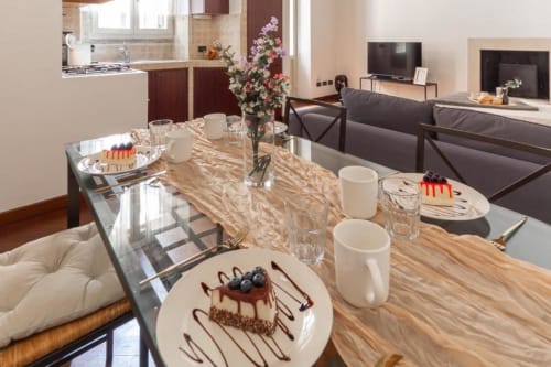 Speisezimmer einer modernen Mailänder Wohnung mit Marmortisch, angerichteten Desserts, frischen Blumen, offener Küche und Wohnzimmer