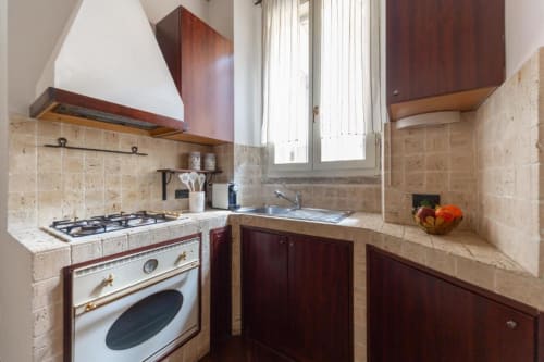 Kompakte Küche mit dunklen Holzschränken, Travertinspritzschutz, Gasherd und Spüle in Mailänder Wohnung