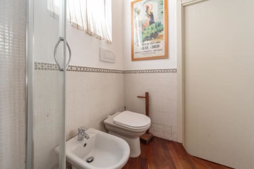 Modernes Badezimmer in Magnolia Apartments Mailand mit weißem Bidet, Toilette, Waschbecken und Glasduschabtrennung auf Holzboden