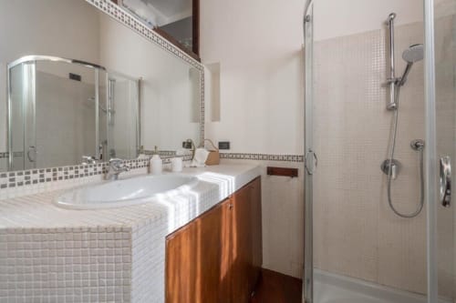 Modernes Badezimmer in den Magnolia Apartments Mailand mit weißen Fliesen, Holzwaschbecken, Spiegel und verglaster Dusche mit Handbrause