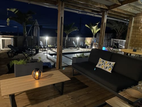 Lounge élégant de nuit à la Villa Des 4 Sens, villa Mafate avec canapé noir, table en bois et vue sur la piscine donnant sur la terrasse illuminée