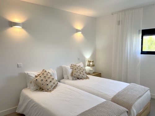 Quarto duplo da villa Casa Tonel em Bordeira com vista para o mar, roupa de cama branca, almofadas decorativas, arandelas e cortinas translúcidas