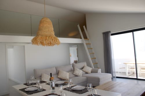 Área de jantar de villa moderna com luminária de fibra trançada, sofá cinzento e vista para o mar em Bordeira, Portugal