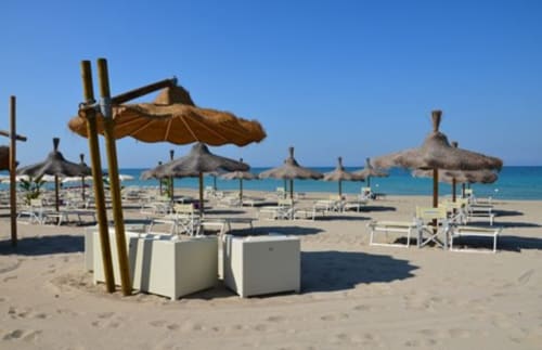 Spiaggia sabbiosa della Masseria Picca Picca con ombrelloni in paglia, lettini e mare cristallino a Morciano di Leuca