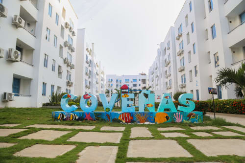 Colorido letrero COVEÑAS con arte temático marino frente a edificios de apartamentos blancos en el hotel Olamar Living, Coveñas Colombia