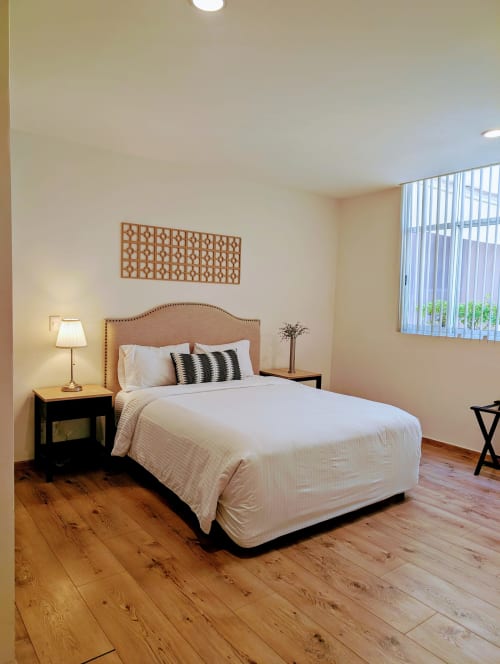 Dormitorio luminoso en Casa Donceles con cabecero de madera, ropa de cama blanca y piso de madera en apartamento de la Ciudad de México