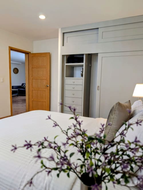 Habitación moderna en Casa Donceles, Ciudad de México, con cama blanca, flores moradas, puerta de madera y armario empotrado.