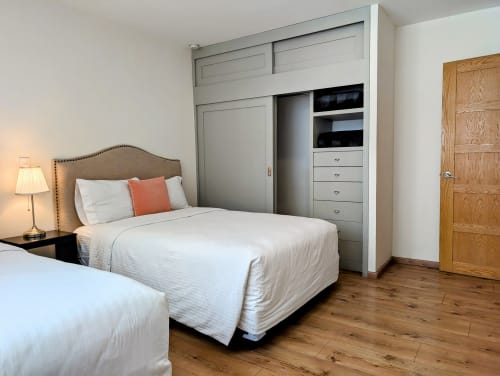 Dormitorio moderno en Casa Donceles, Ciudad de México, con dos camas, armario gris empotrado, piso de madera y vista al patio interior