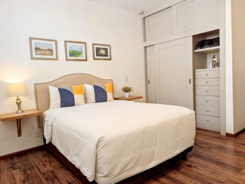 Dormitorio luminoso en Casa Donceles Ciudad de México con cama tapizada en beige, almohadas azul marino y amarillo, mesita de noche de madera