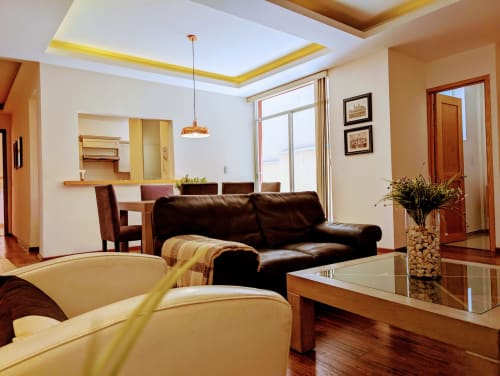 Sala moderna del apartamento Casa Donceles en la Ciudad de México con sofá de cuero negro, detalles de techo amarillo y zona de comedor