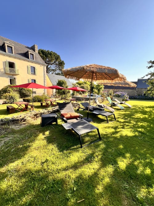 Jardin ensoleillé aux Logis de Kergoulou à Concarneau avec transats, parasols et maison jaune