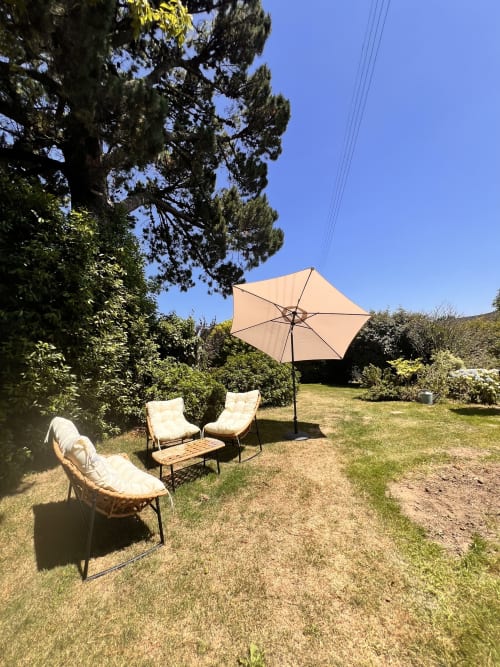 Coin de détente du jardin aux Logis de Kergoulou à Concarneau avec parasol beige et chaises rembourrées