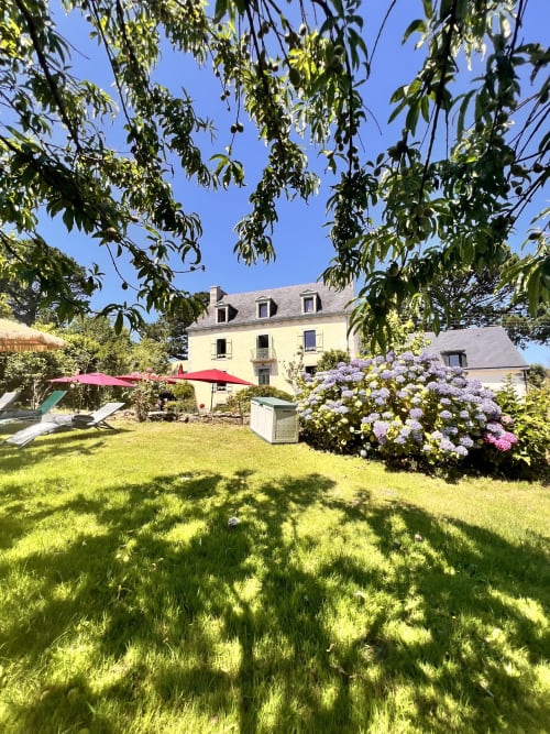 Le jardin des logis de Kergoulou à Concarneau avec hortensia en fleur, pelouse et villa en pierre