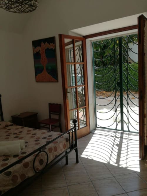 Luminosa camera da letto con letto in metallo, opere d'arte e porte-finestre che si aprono sul giardino di Zia Amalia Villa Asfodelo, Alghero