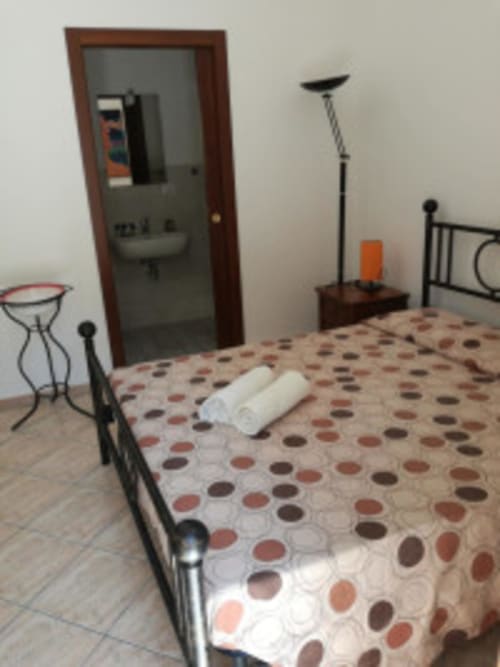 Camera da letto di Villa Asfodelo Zia Amalia ad Alghero con biancheria a pois, letto in ferro e vista sul giardino