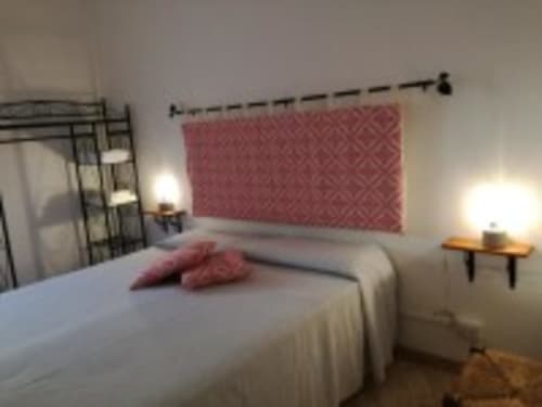 Camera luminosa con letto bianco, testata rossa trapuntata e vista sul giardino di Zia Amalia Villa Asfodelo ad Alghero
