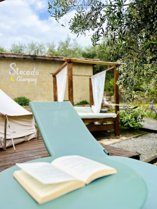 Livre ouvert sur transat turquoise au jardin de l'agritourisme Stecadò à Dolceacqua, Italie, avec tente et pergola en arrière-plan