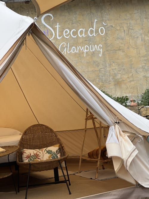 Intérieur de la tente glamping Stecadò avec fauteuil en rotin et draperies blanches à Dolceacqua