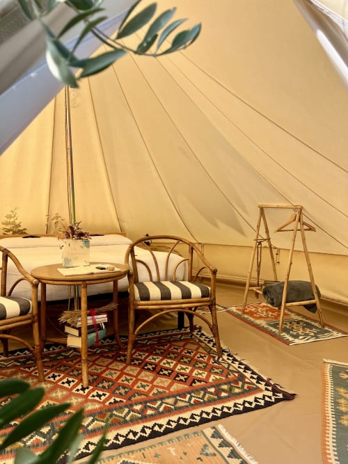Intérieur de tente glamping à Agritusmo Stecadò avec chaises en rotin, table en bois et tapis à motifs à Dolceacqua