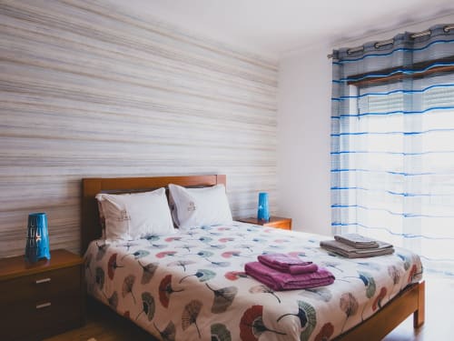Modern bedroom in Baleal Beach Holiday Villa, Óbidos, with patterned bedding, wooden furniture, and blue striped curtains