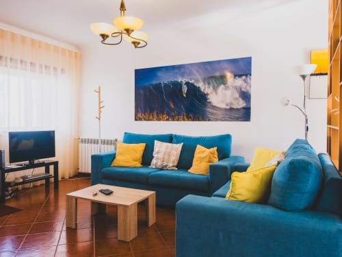 Cozy living room at Baleal Beach Holiday Villa with blue sofas, yellow pillows, and large wave artwork overlooking Bombarral