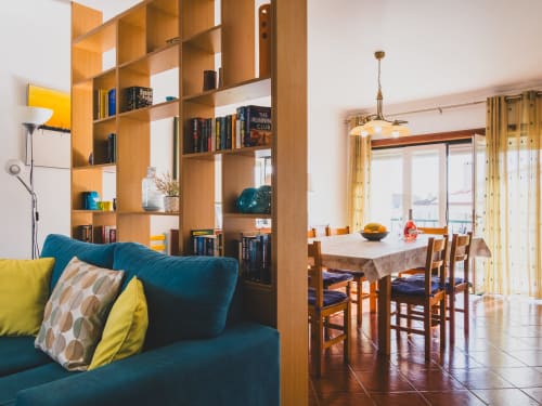 Open-plan living area in Baleal Beach Holiday Villa with teal sofa, wooden shelving, dining table, and sea views through