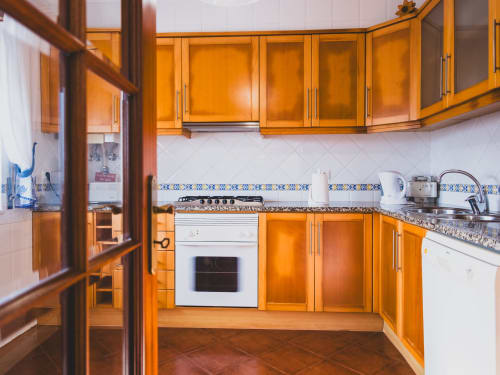 Warm wooden kitchen with orange cabinets, white oven, and blue tile accents at Baleal Beach Holiday Villa