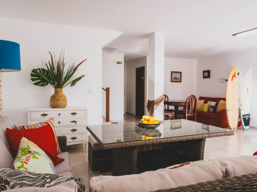 Bright villa living room with sea views, wicker coffee table, colorful pillows, surfboards, and wooden furniture at Baleal