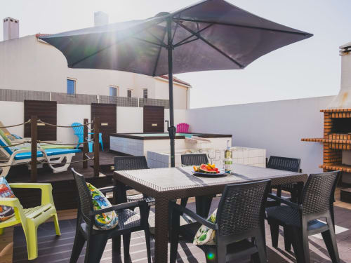 Sunny rooftop terrace at Baleal Beach Holiday Villa with black dining table, umbrella, and lounge chairs overlooking the sea