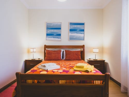 Quarto da Baleal Sunset Residence com vista para o oceano, cama em madeira, roupa de cama laranja e abajures gémeos em Bombarral, Portugal