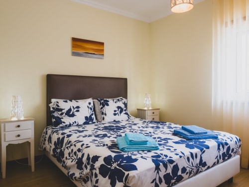 Quarto da villa Baleal Sunset Residence em Bombarral com roupa de cama floral azul, cabeceira escura e paredes amarelas