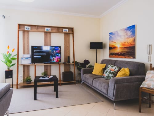 Sala de estar moderna da villa Baleal Sunset Residence com sofá cinzento, almofadas amarelas, quadro com vista para o oceano ao pôr do sol, madeira