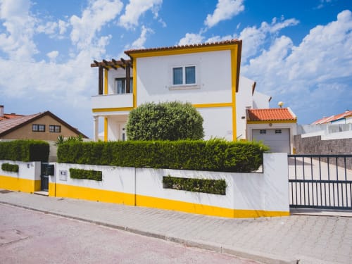 Baleal Sunset Residence villa in Bombarral with yellow and white facade, green landscaping, and ocean views in Óbidos,
