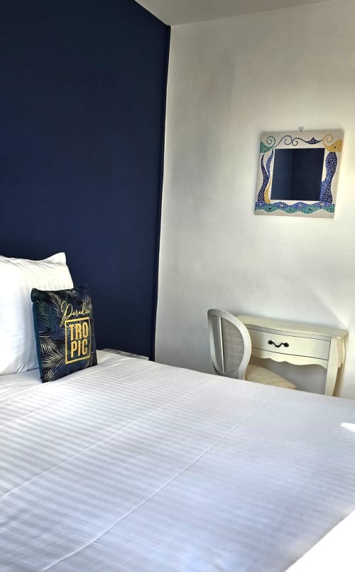 Modern bedroom at Hôtel De La Fontaine in Nice with navy accent wall, white bedding, and decorative blue tile mirror