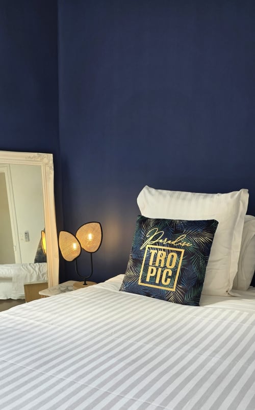 Stylish hotel bedroom at Hôtel De La Fontaine in Nice with navy walls, decorative pillow, woven lamps, and mirror
