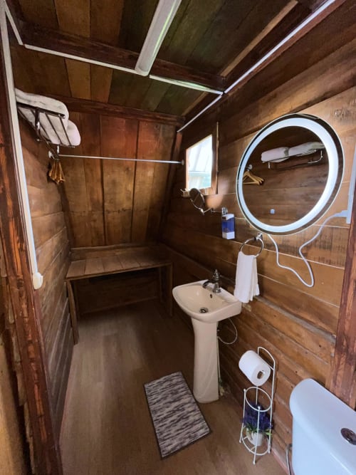 Modern bathroom in Chalet Vistas del Poas villa with circular LED mirror, pedestal sink, wooden walls, and shower area in