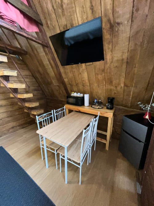 Cozy chalet dining area with wooden beams, white chairs, dining table, mounted TV, and kitchen counter at Chalets Vistas del