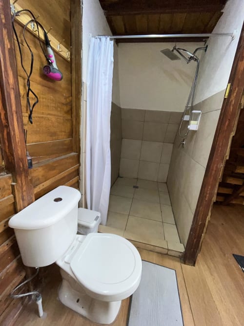 Modern bathroom with white toilet, tiled shower enclosure, and wooden walls at Chalets Vistas del Poas villa in Heredia,