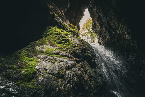 Formación rocosa cubierta de musgo dentro de la cueva Cuevas de Viñayo con cascada y abertura de luz natural