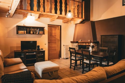 Sala de estar rústica en Casa Rural Sensaciones con vigas de madera, chimenea y asientos naranjas en Cuevas de Viñayo