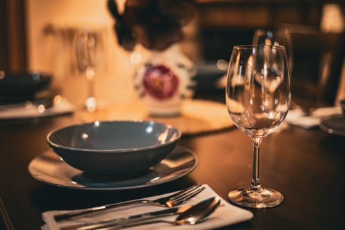 Elegante montaje de mesa en la villa Casa Rural Sensaciones con cuenco oscuro, copa de vino y cubertería sobre mesa de comedor iluminada calurosamente