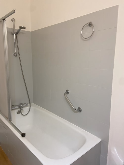 Salle de bains moderne avec carrelage blanc, baignoire, douche et barres de sécurité à l'Hôtel De La Bonnheur à Bracieux, France